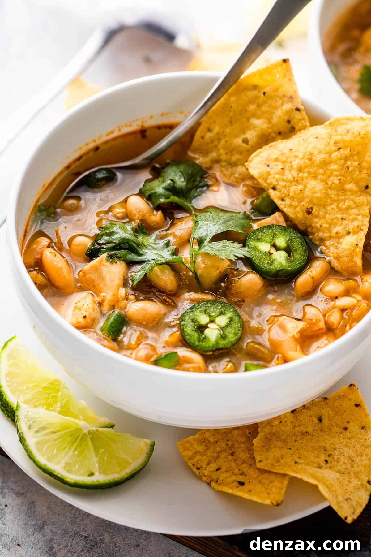 side shot of a chicken chili in a bowl topped with jalapenos and tortilla chips