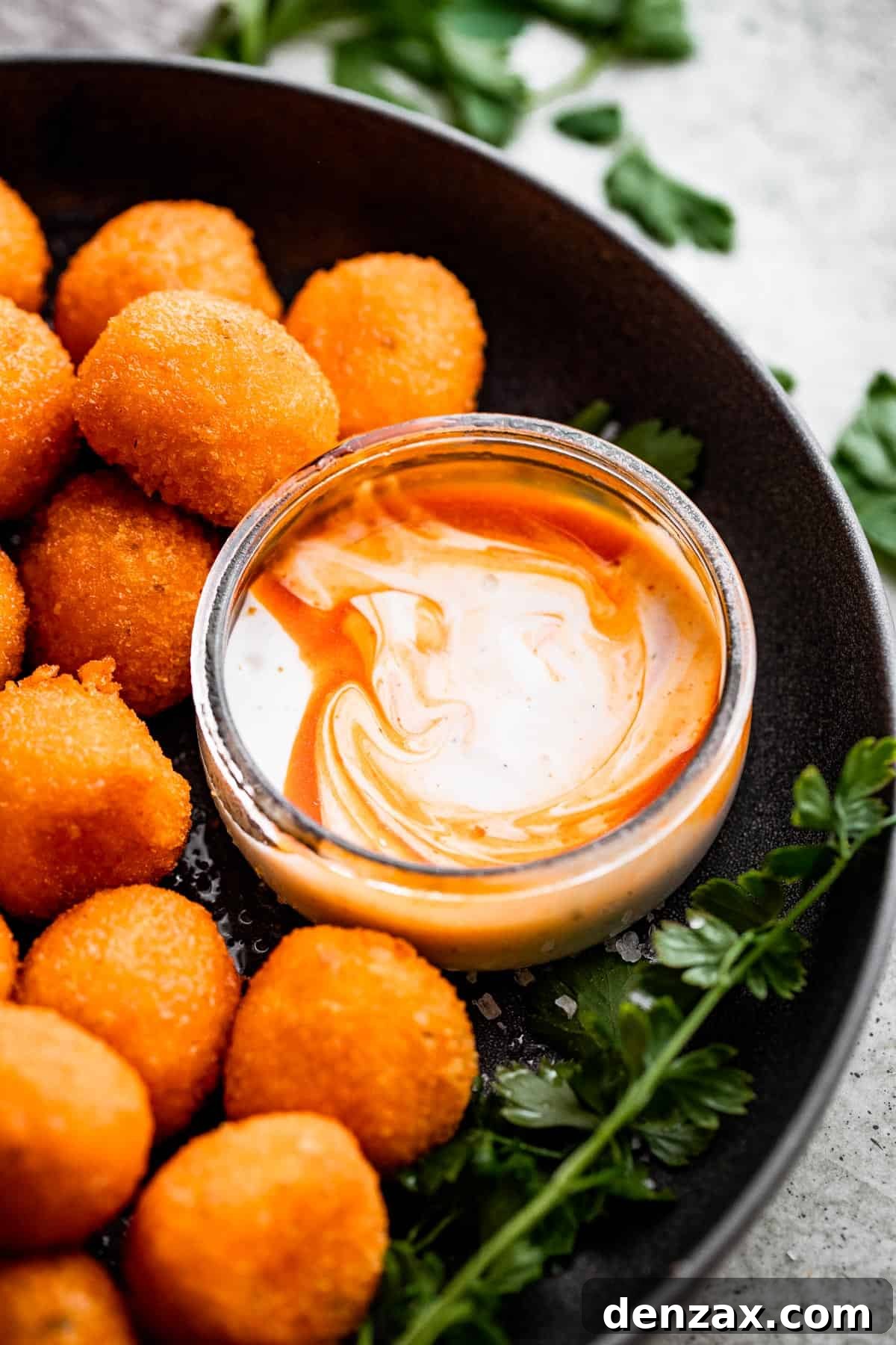 a black serving bowl with air fried jalapeno popper balls and a smaller glass bowl with dipping sauce.