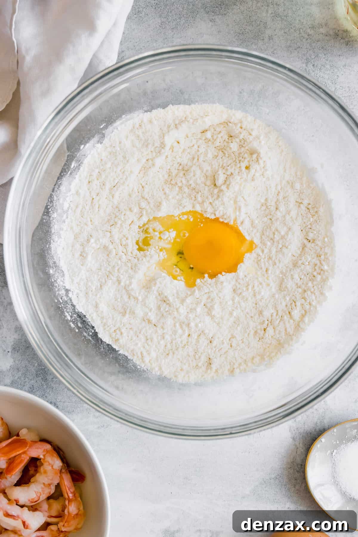 A Glass Bowl Containing the Dry Tempura Ingredients with a Cracked Egg in the Center
