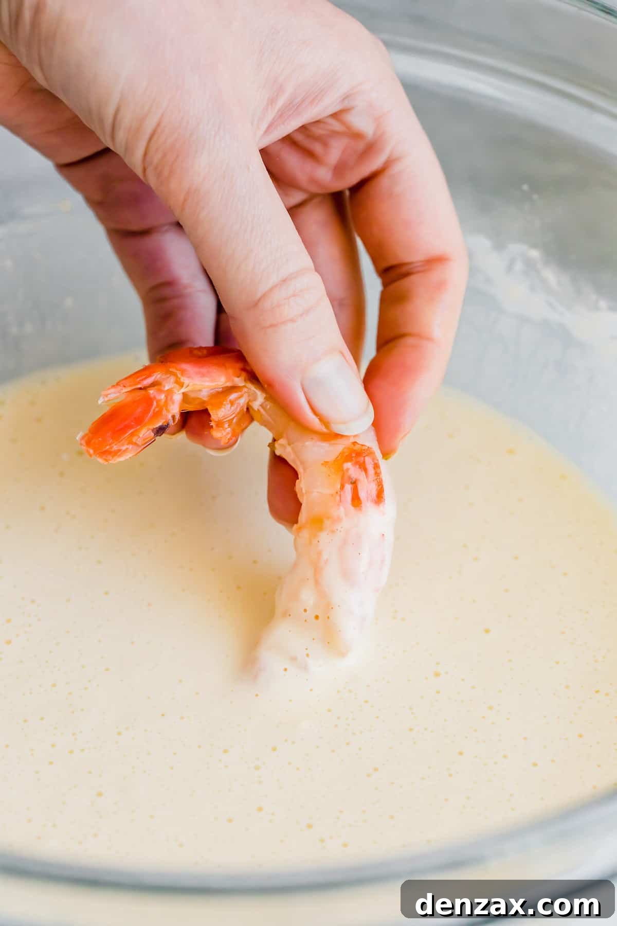 A Raw Shrimp Being Dunked Into a Bowl of Tempura Batter