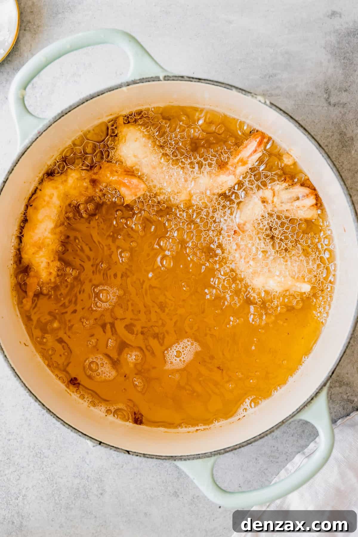 Three Shrimp Frying in a Pastel Pot with a White Towel Next to it