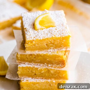 four lemon bars stacked one on top of the other and finished with a dusting of powdered sugar and a slice of lemon on top
