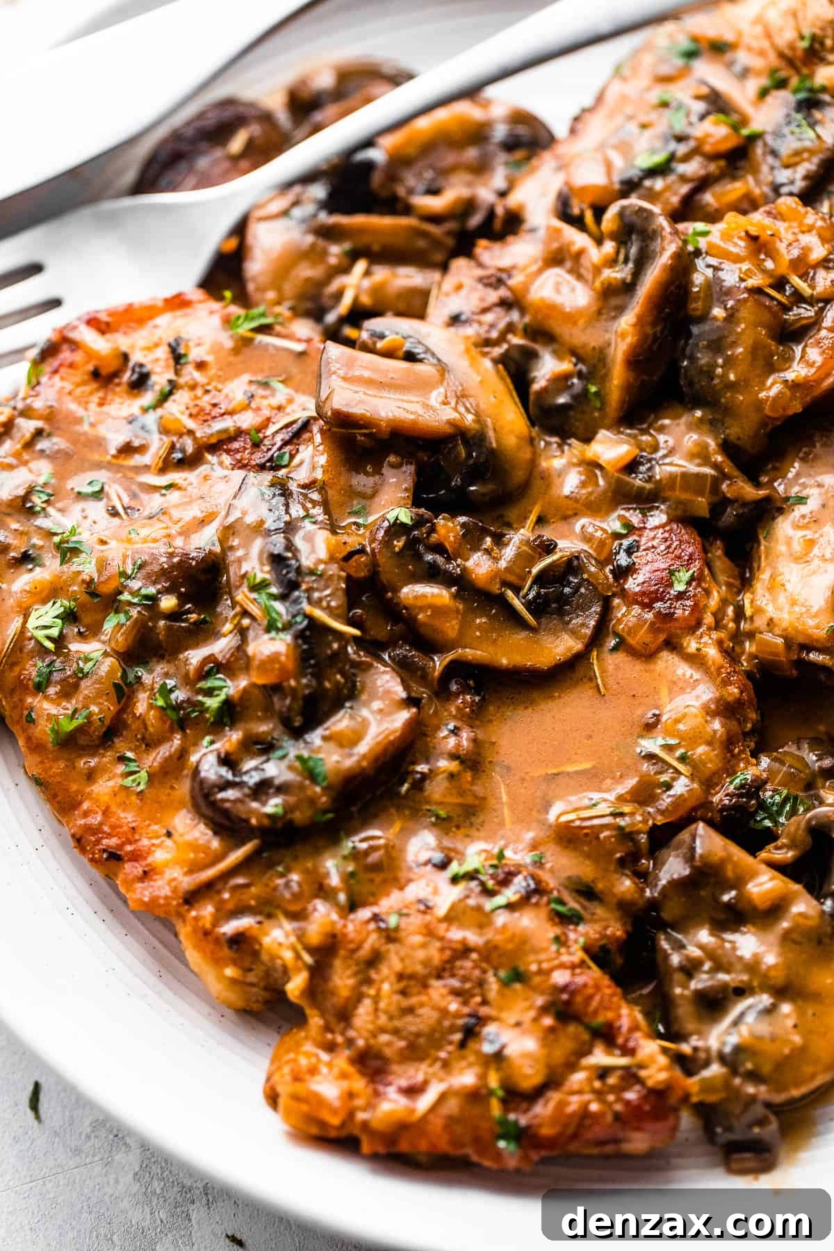 two bone in pork chops served on a white plate and topped with creamy mushroom gravy