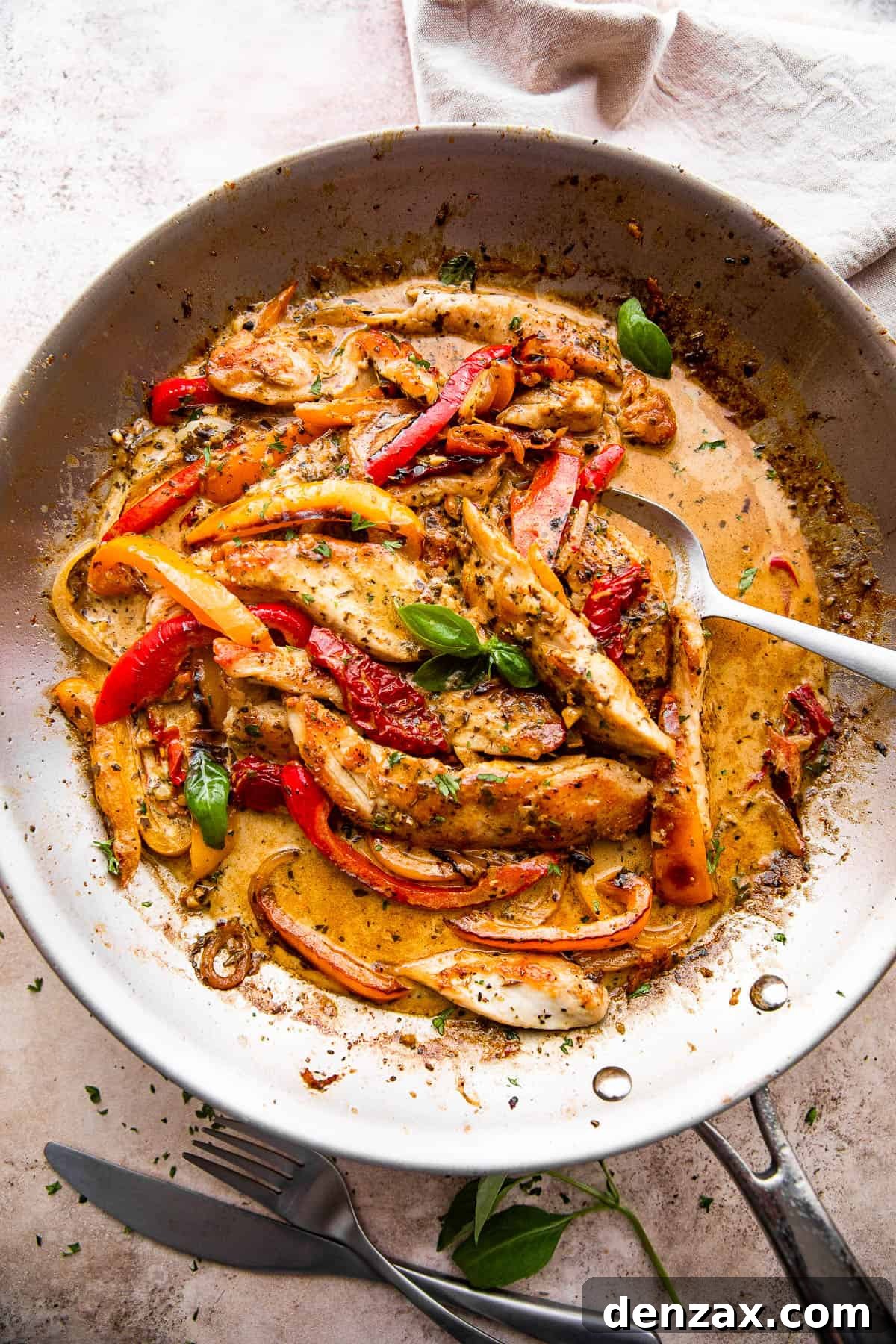overhead shot of a skillet with creamy pesto chicken strips, peppers, and cream sauce