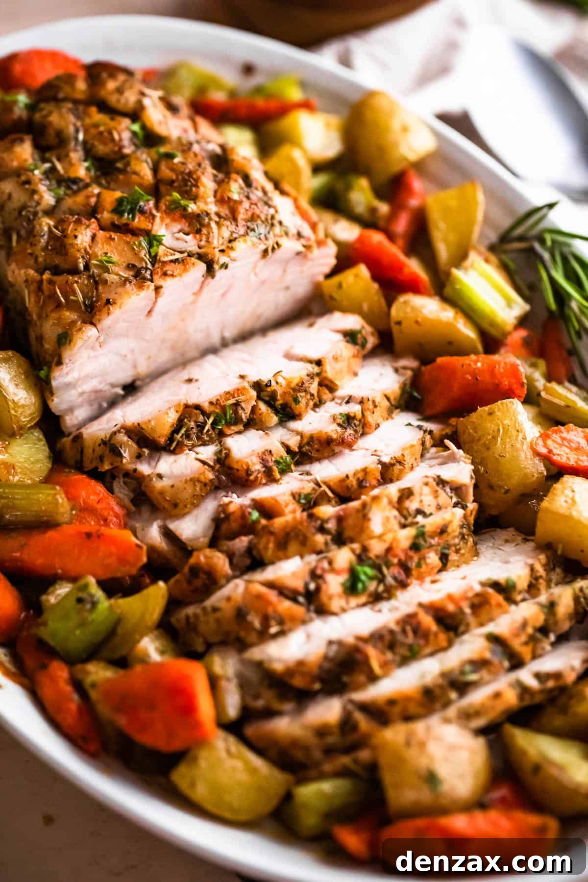 Herb-Roasted Pork Loin with Garlic Vegetables 2 side shot of oval plate with cooked and sliced pork loin roast and roasted vegetables arranged around the roast