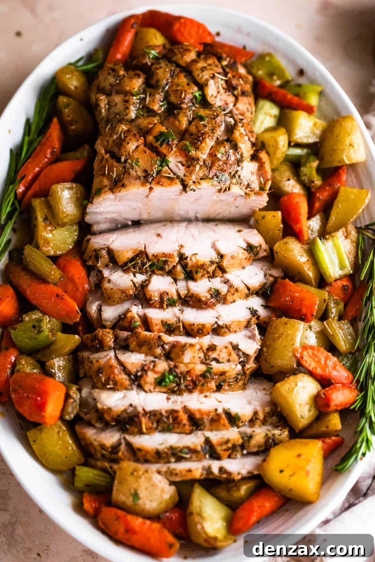 Herb-Roasted Pork Loin with Garlic Vegetables 3 overhead shot of oval plate with cooked and sliced pork loin roast and roasted vegetables arranged around the roast