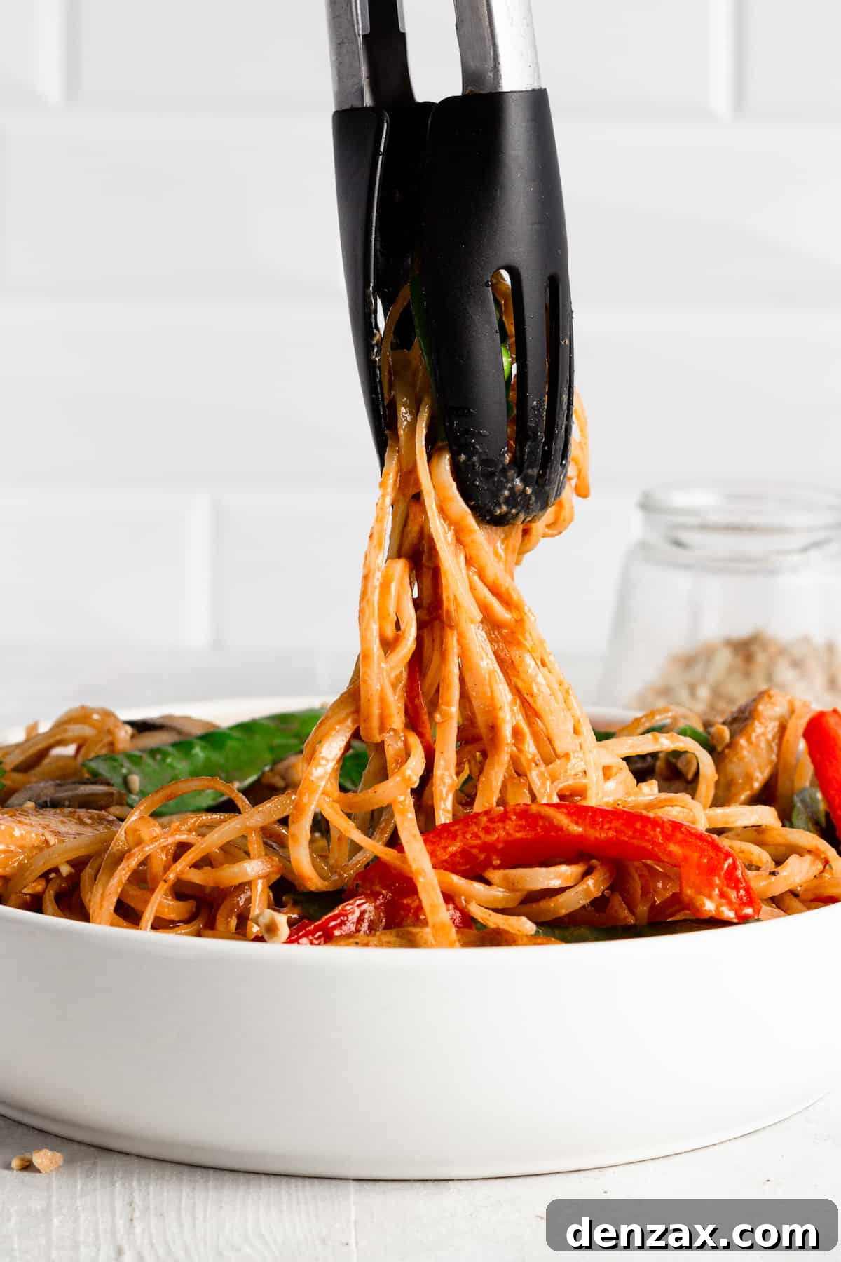 Tongs Scooping Up Some Noodles Out of a Bowl of Chicken Lo Mein