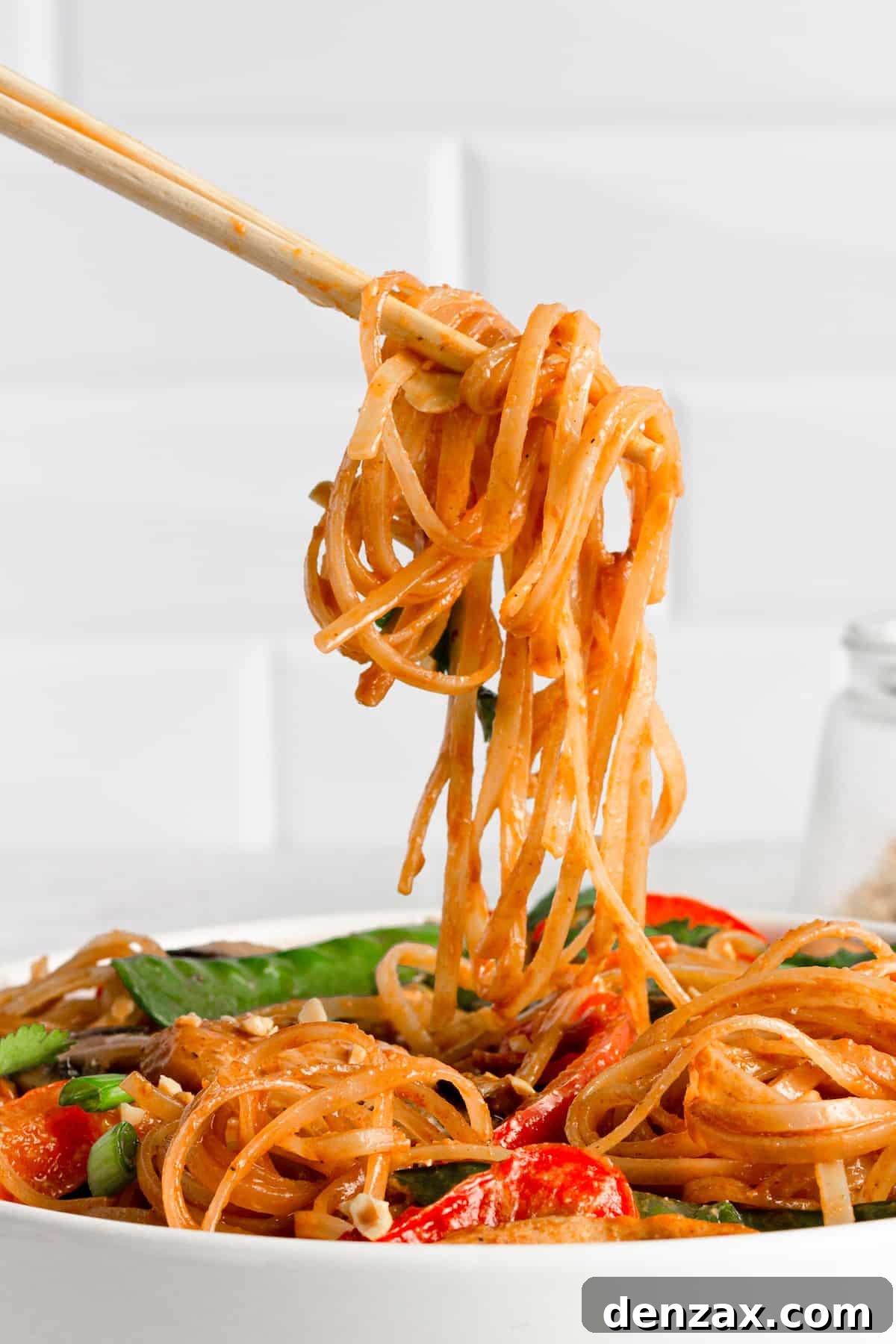 A Pair of Chopsticks Holding a Bite of Chicken Lo Mein Over the Bowl