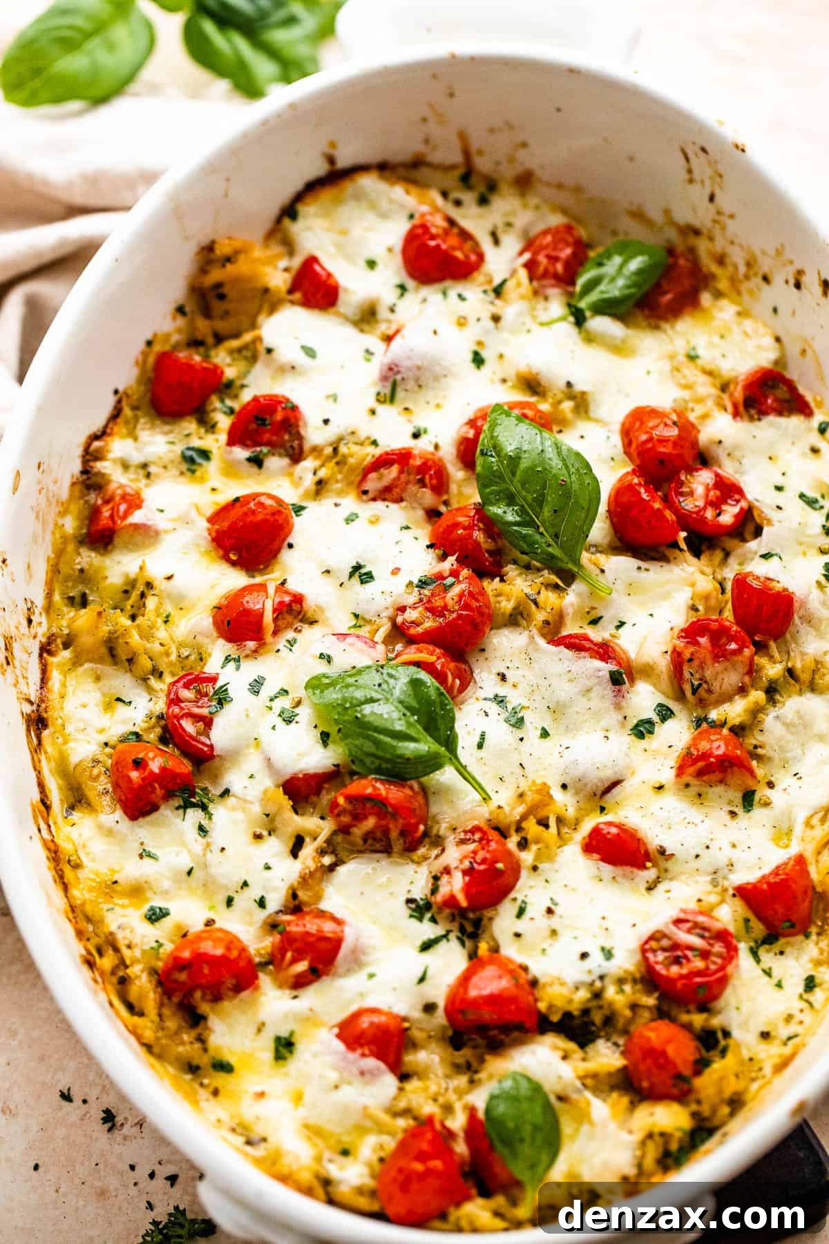 chicken caprese casserole in a white baking dish topped with basil leaves and cherry tomatoes