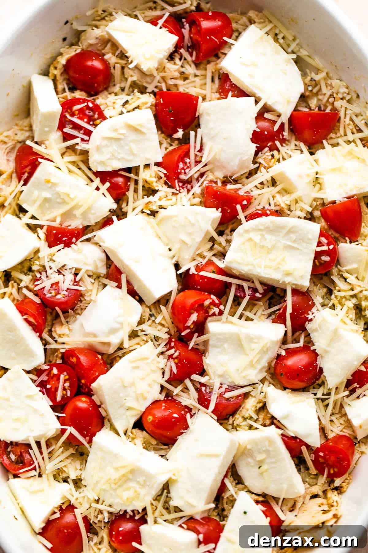 chicken caprese casserole in a white baking dish topped with fresh mozzarella chunks and cherry tomatoes