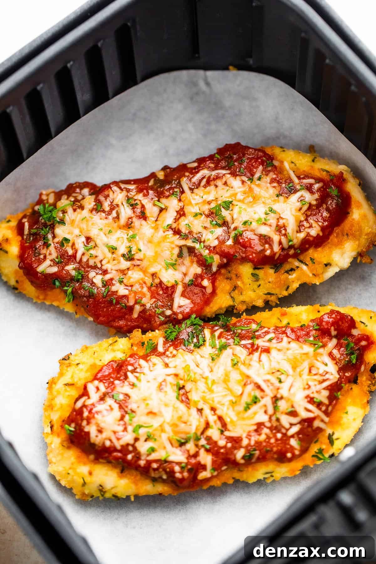 Two Pieces of Breaded, Partially Cooked Chicken Being Topped with Marinara and Shredded Parmesan Cheese
