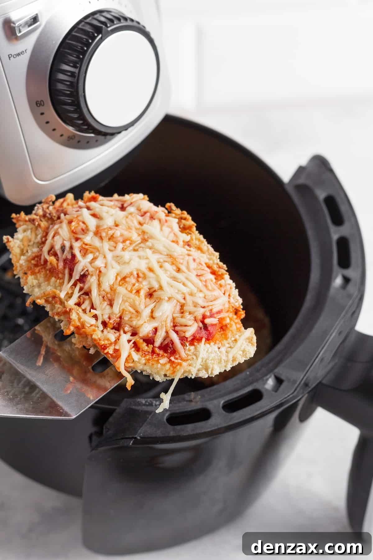 A Piece of Chicken Parm on a Metal Spatula Hovering Above an Air Fryer Basket