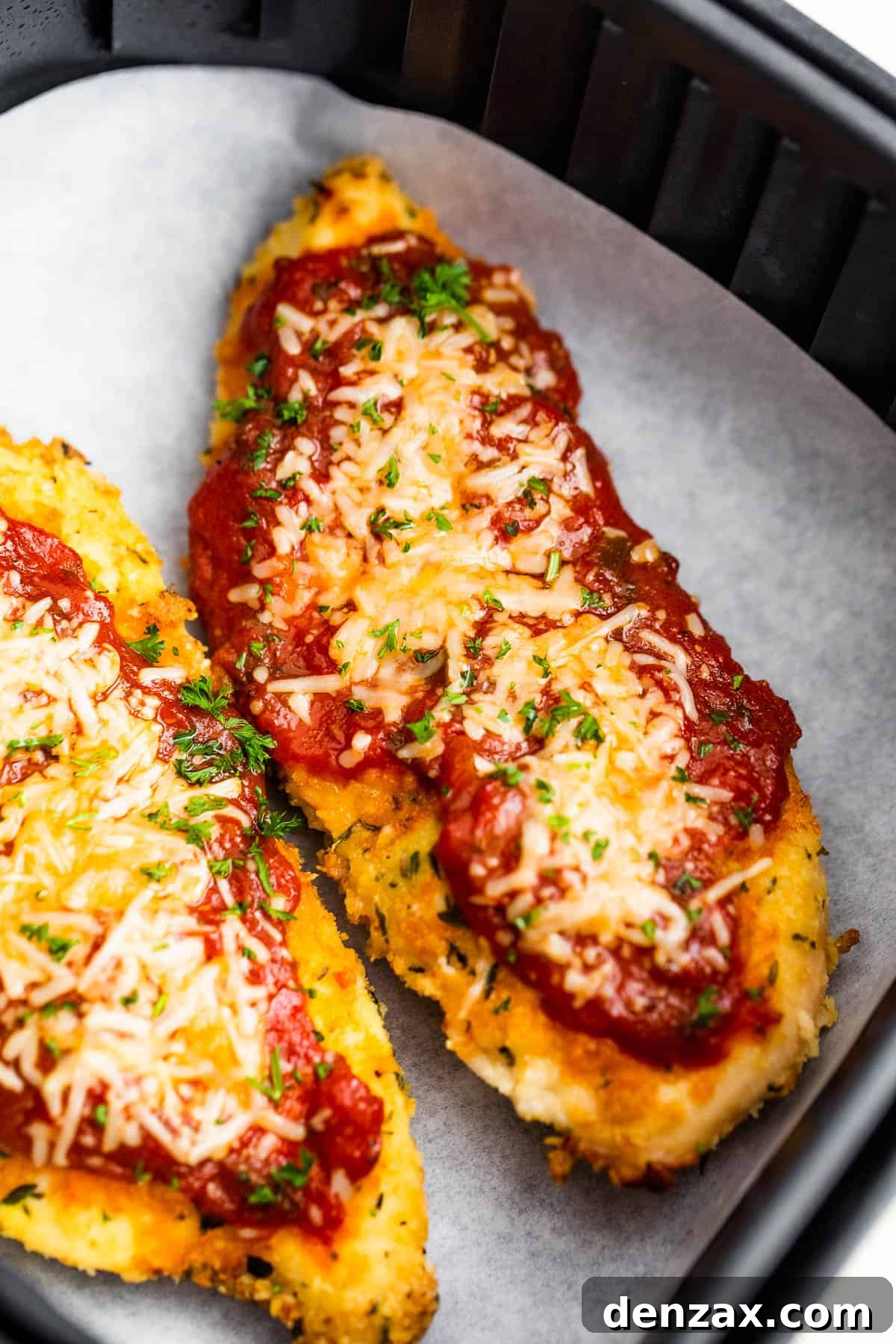 Two Pieces of Breaded, Partially Cooked Chicken Being Topped with Marinara and Shredded Parmesan Cheese