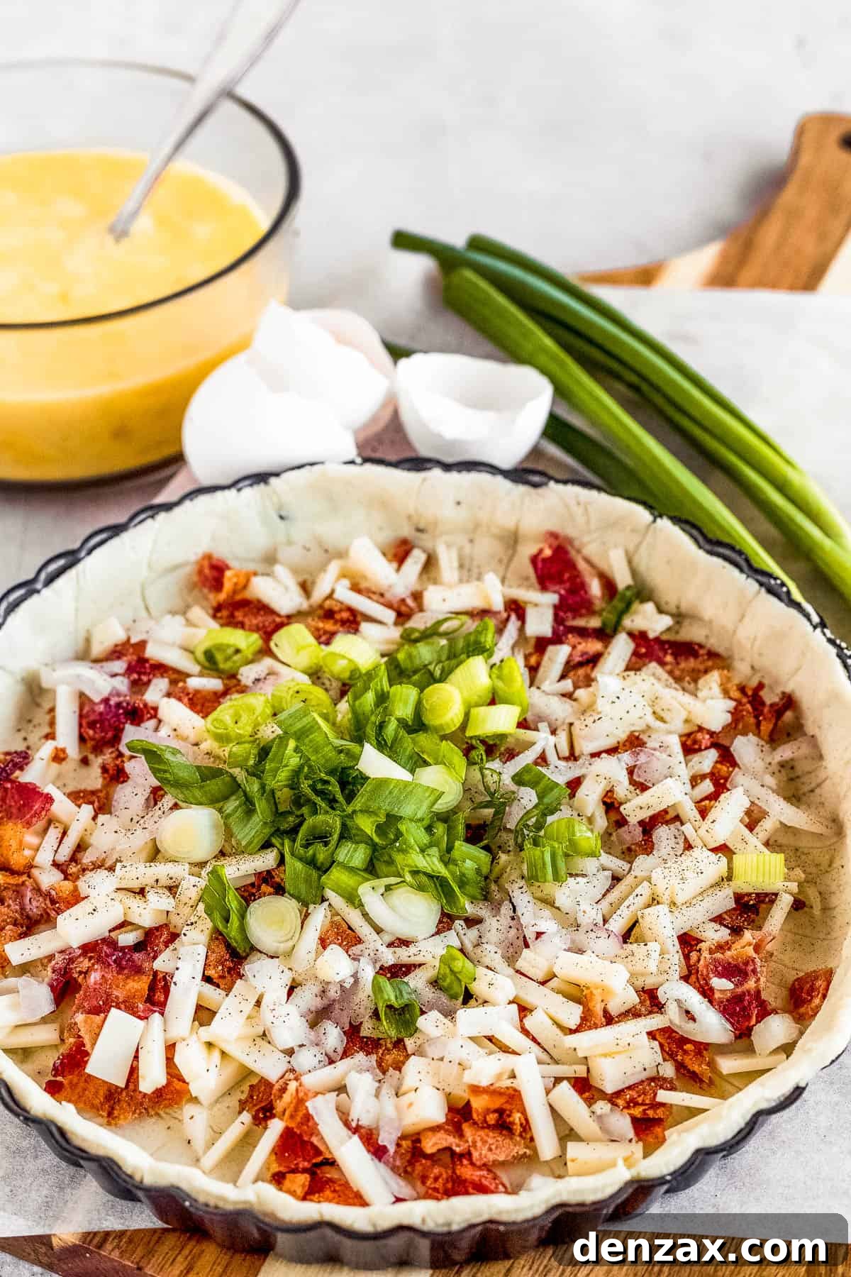 Chopped Onions, Shallots and Bacon Bits Inside of a Pie Crust with the Egg Mixture in the Background