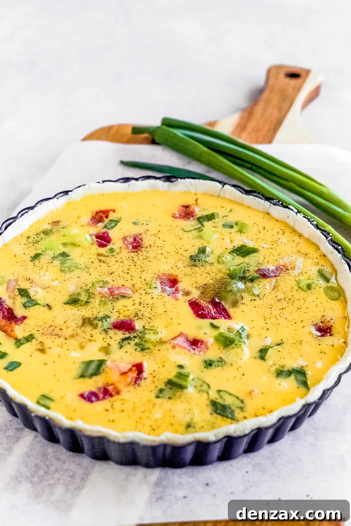 An Unbaked Quiche Lorraine on a Cutting Board Lined with Parchment Paper