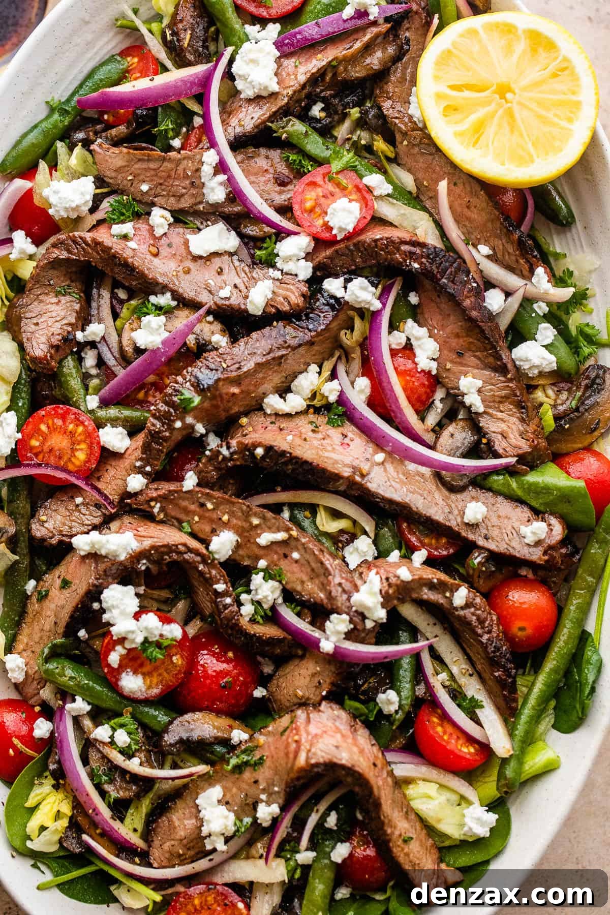 Steak Salad served on a long plate topped with cheese crumbles, tomatoes, and mushrooms