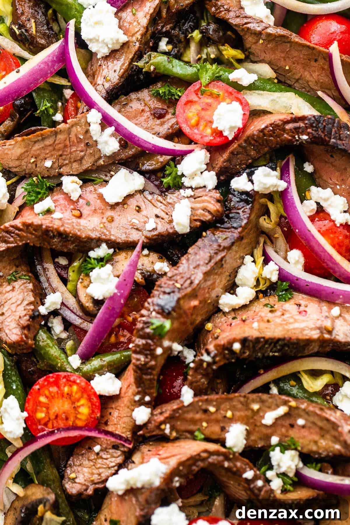 up close photo of Steak Salad on a long plate topped with cheese crumbles, tomatoes, and mushrooms