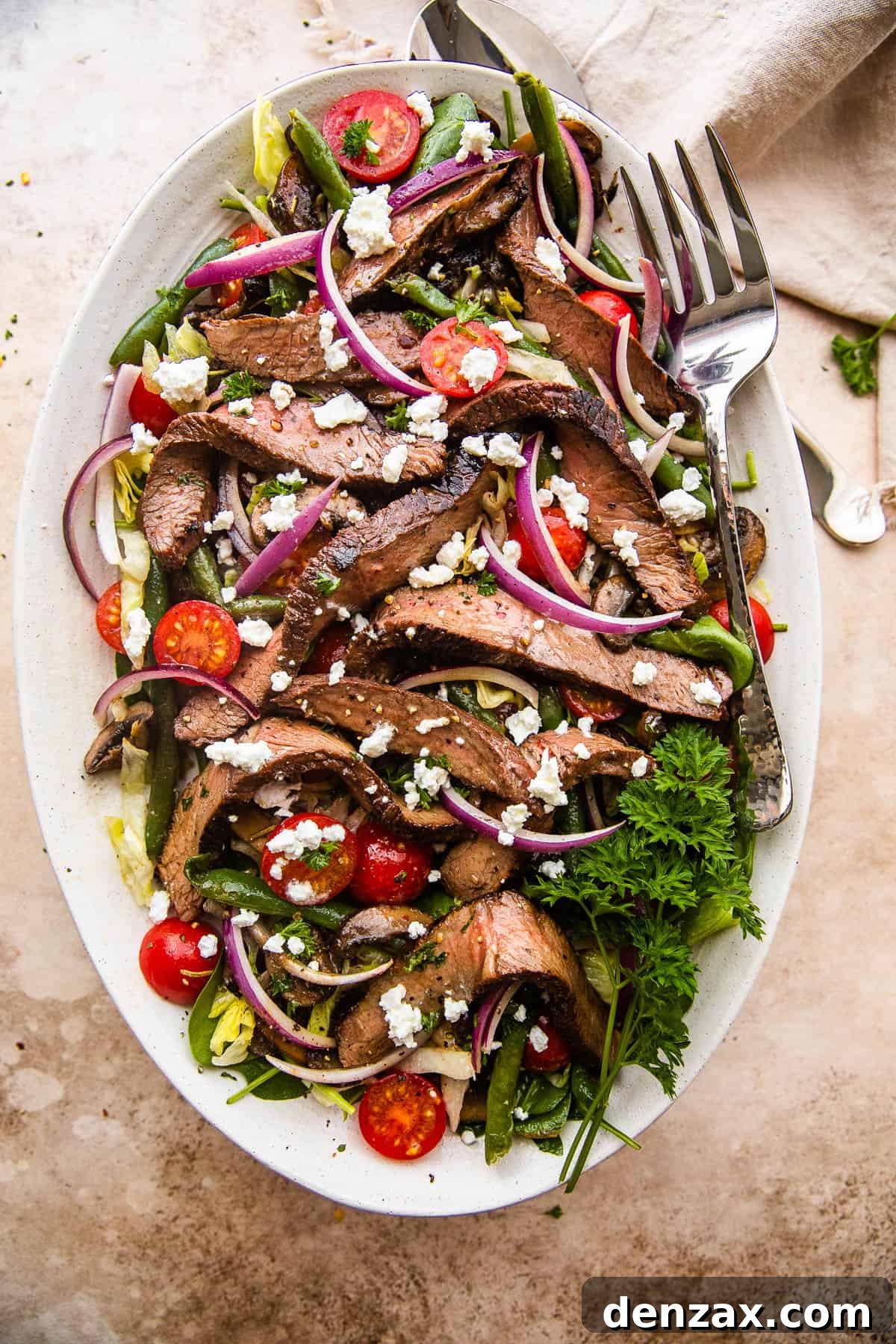 Steak Salad on a long plate topped with cheese crumbles, tomatoes, and mushrooms