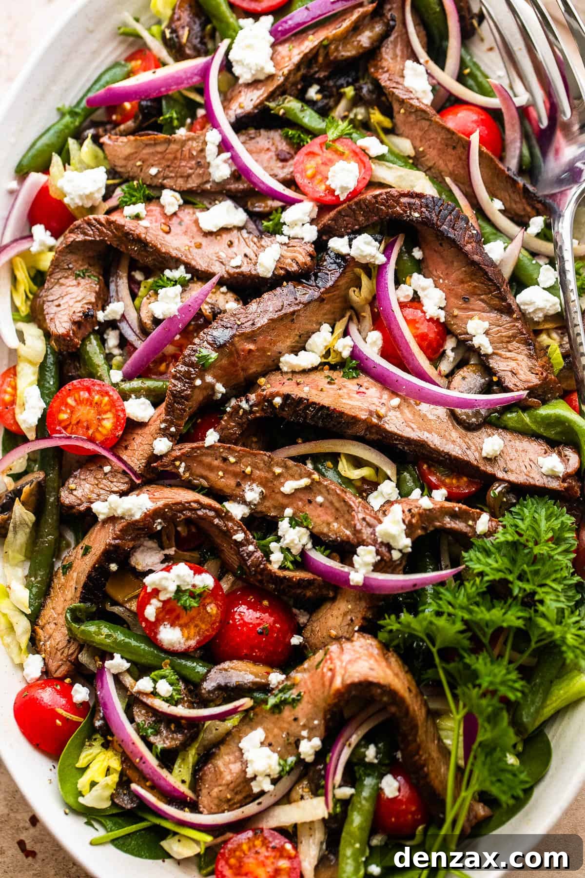 Steak Salad on a long plate topped with cheese crumbles, tomatoes, and mushrooms