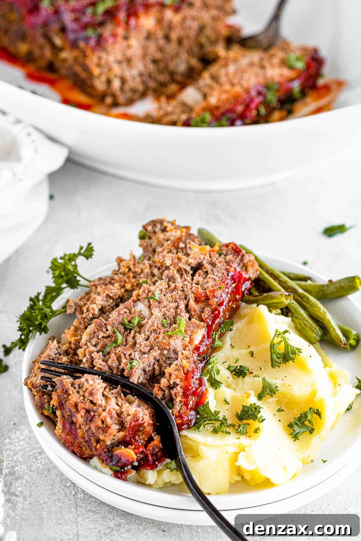 A Fork Digging Into a Slice of Meatloaf on a Plate with Potatoes and Veggies