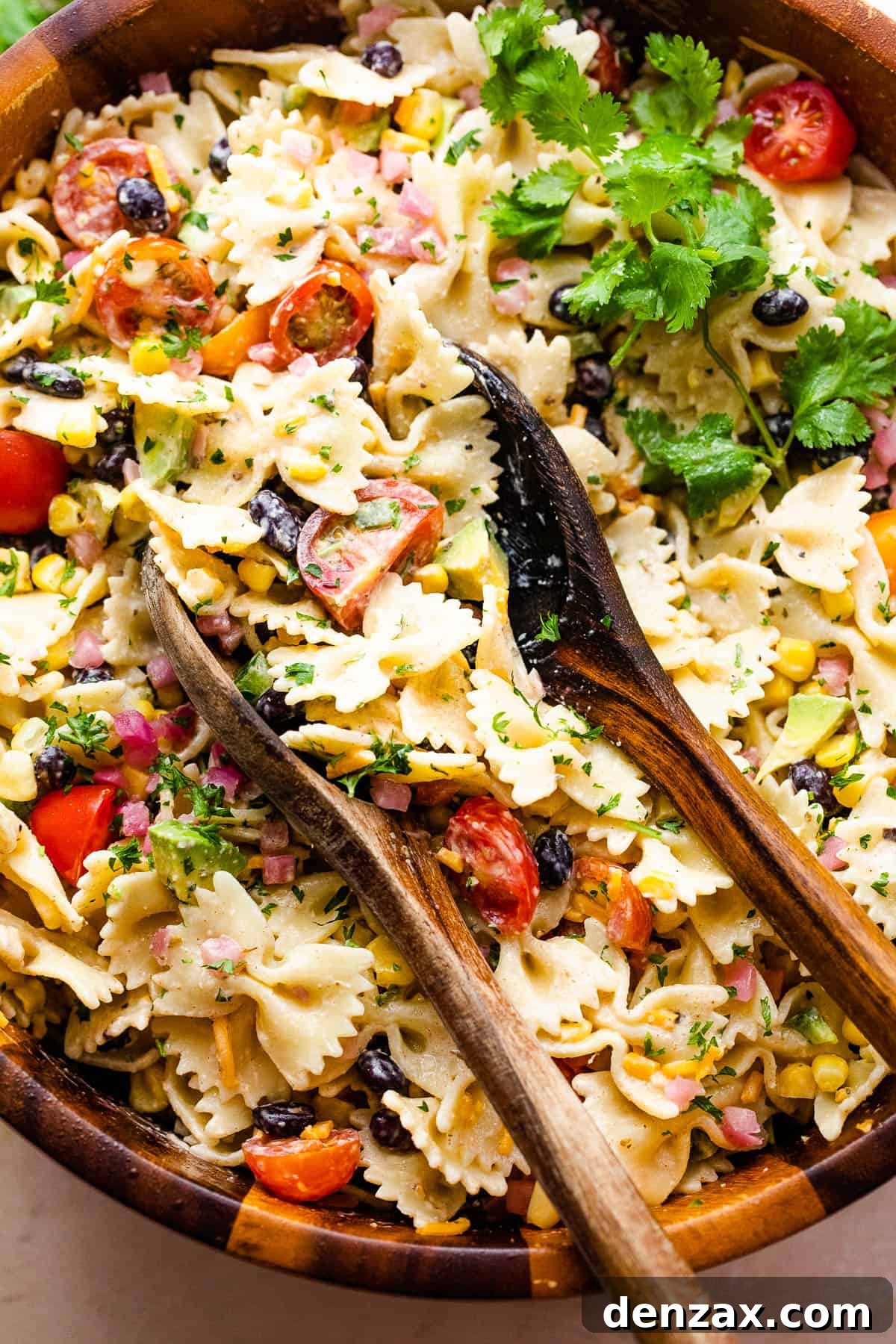 pasta salad in a wooden salad bowl with two wooden spoons