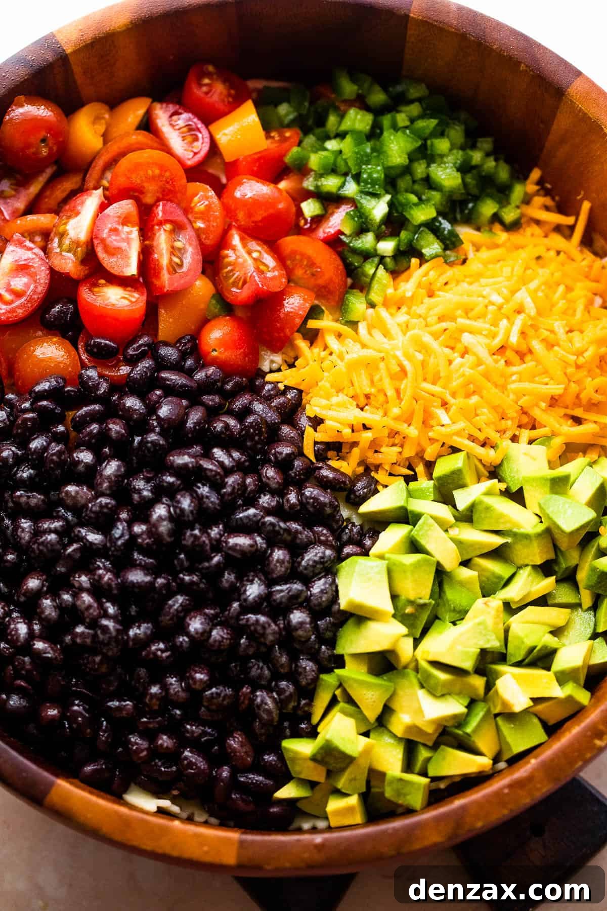 wooden bowl with chopped up tomatoes, avocado, shredded cheese, and black beans