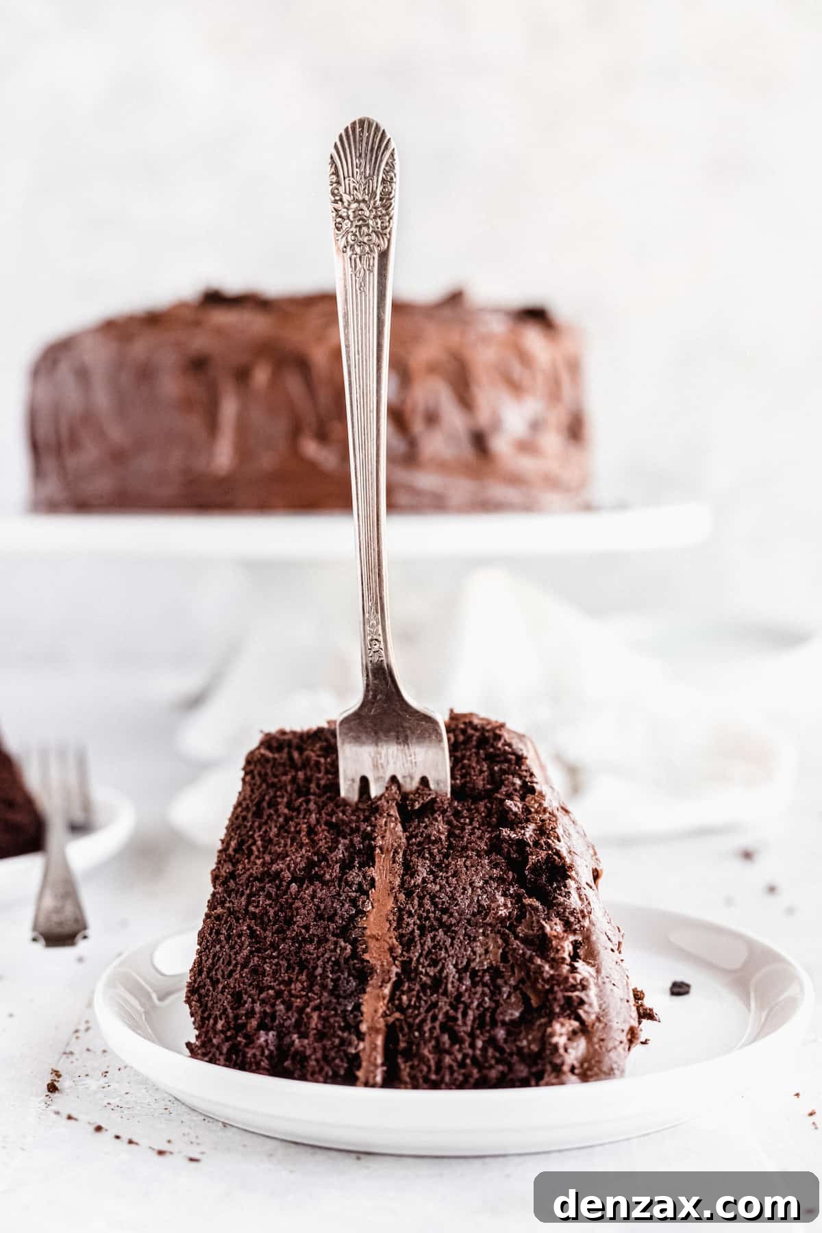 A Slice of Chocolate Cake on a White Plate with a Fork Sticking Into it
