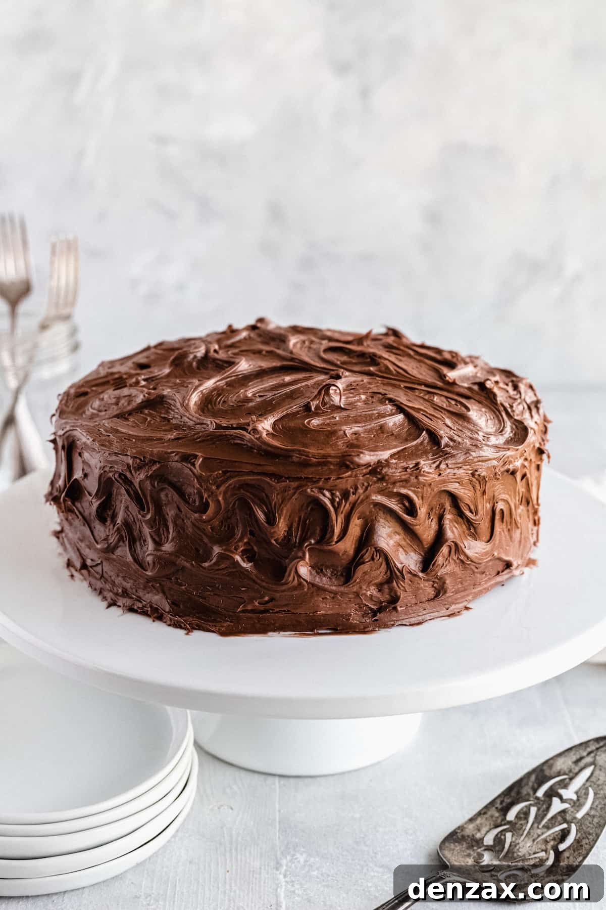 A Frosted Chocolate Cake on a White Stand with a Dessert Spatula in the Foreground
