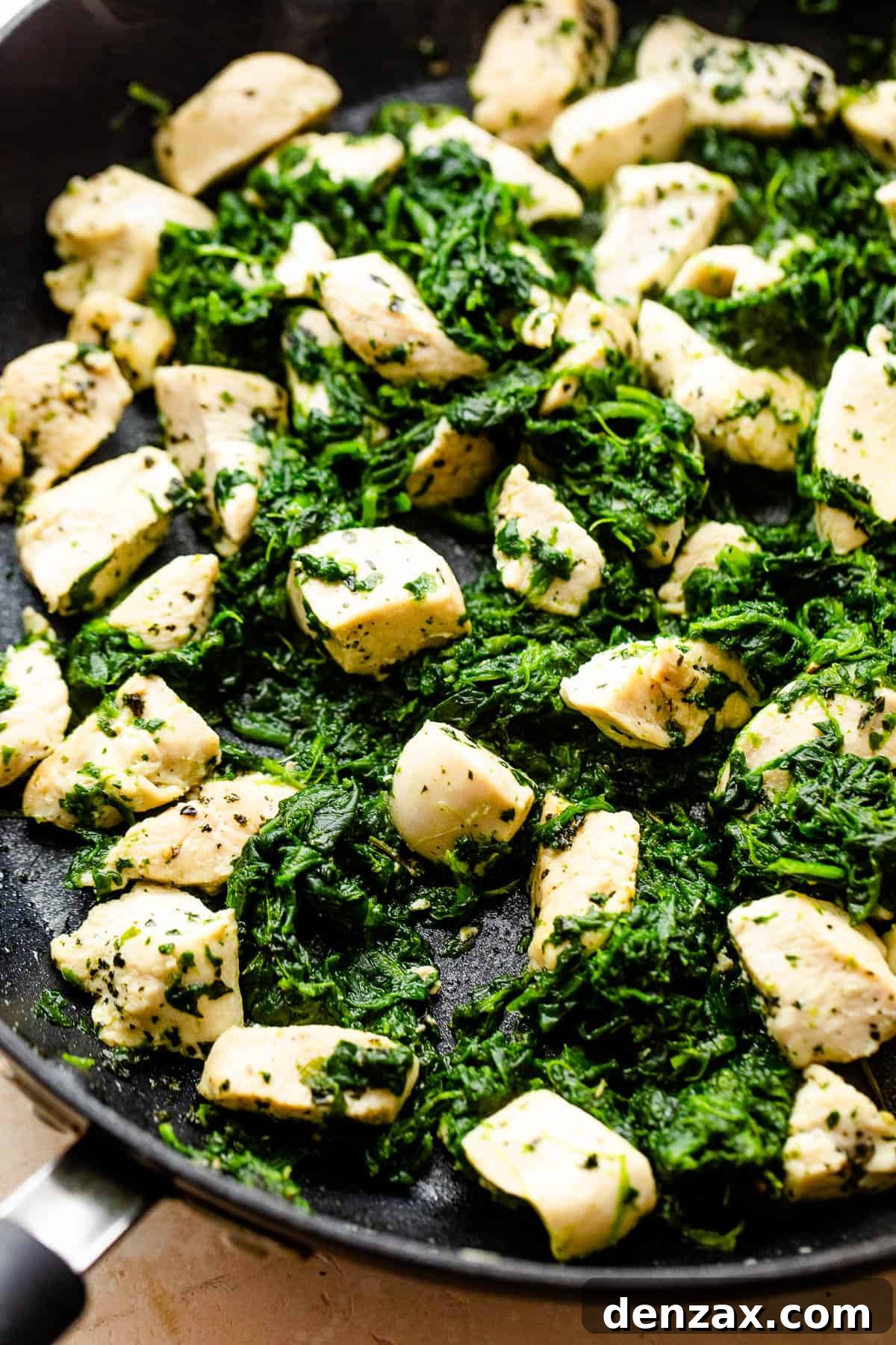 cooking chicken breast pieces and spinach in a black skillet