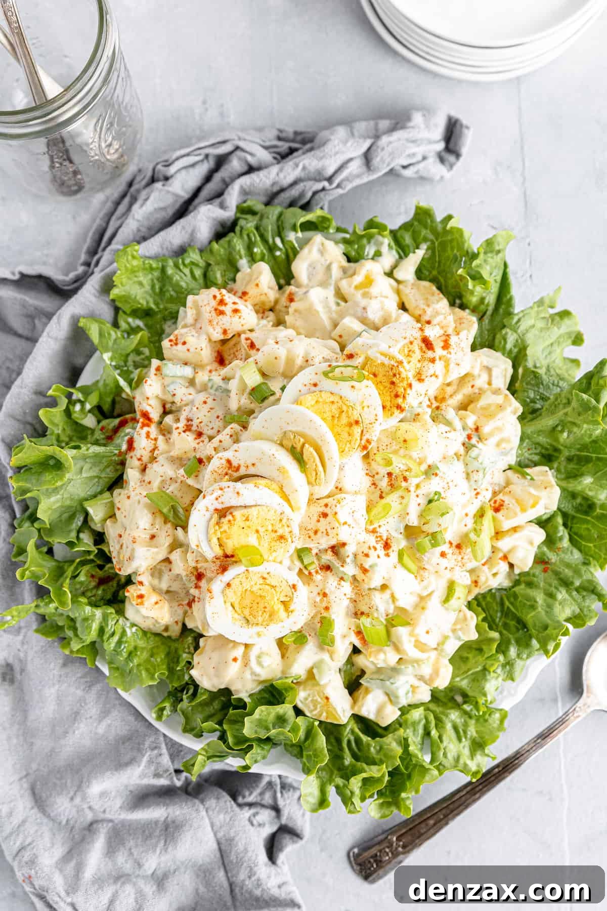 An Overhead Shot of a Potato Salad on a Lettuce-Lined Plate Beside a Gray Kitchen Towel