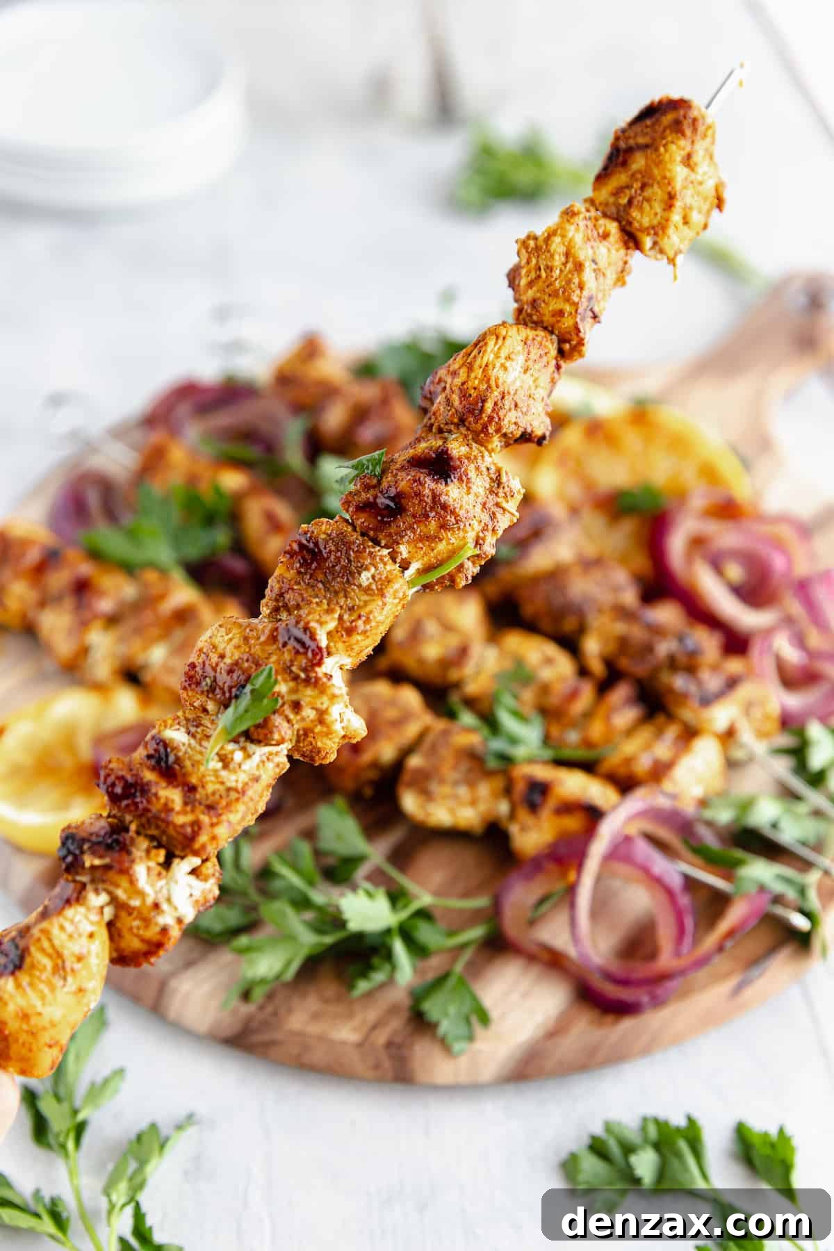 A Shawarma Grilled Chicken Skewer Being Held Above a Platter Containing More Kebabs