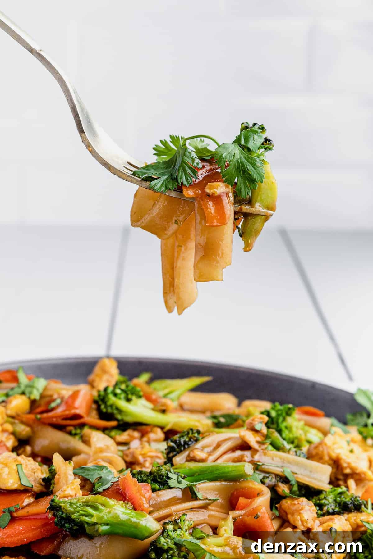 A Bite of Pad See Ew on a Fork Hovering Above a Full Plate
