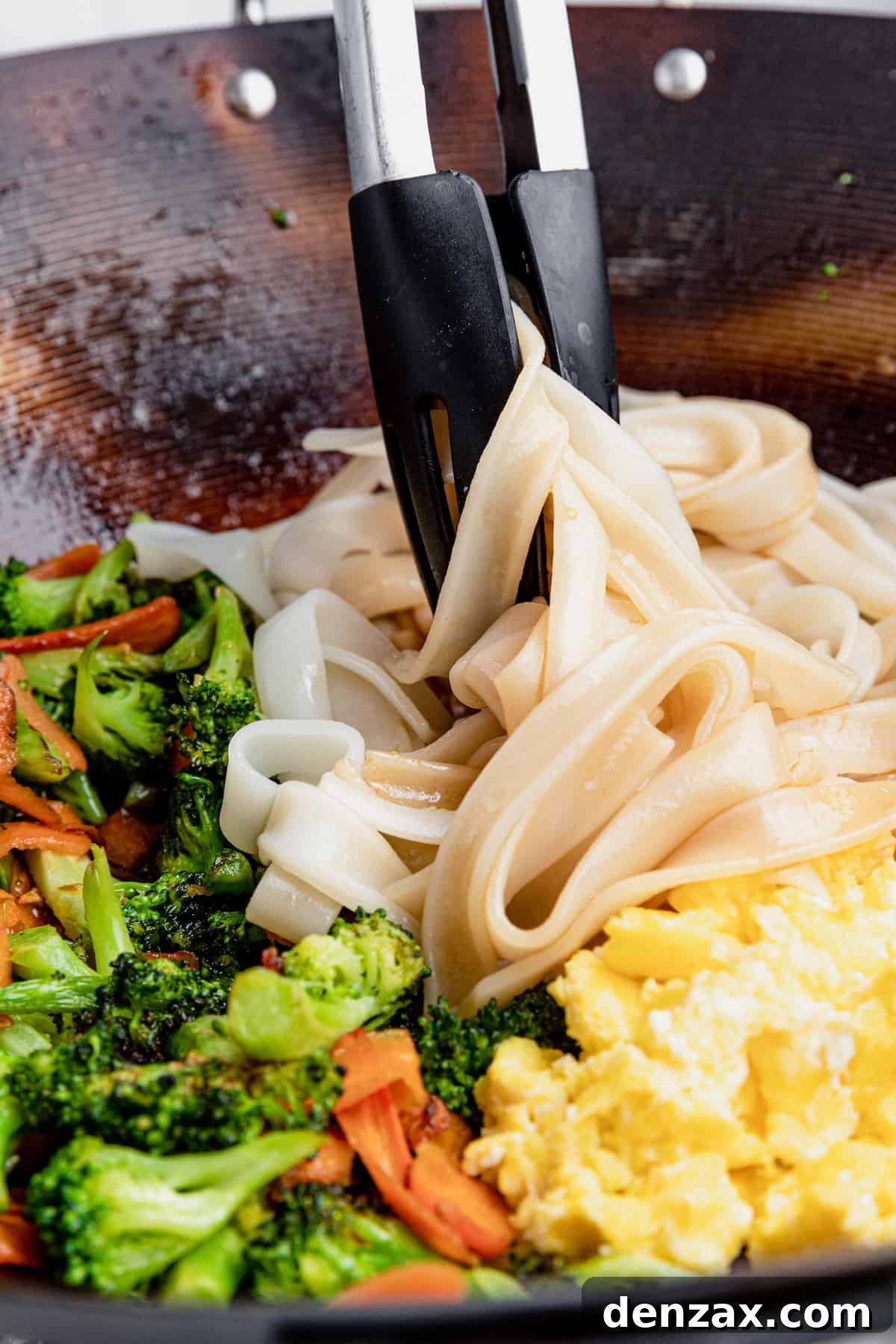 A Pair of Tongs Mixing the Noodles with the Eggs and Vegetables
