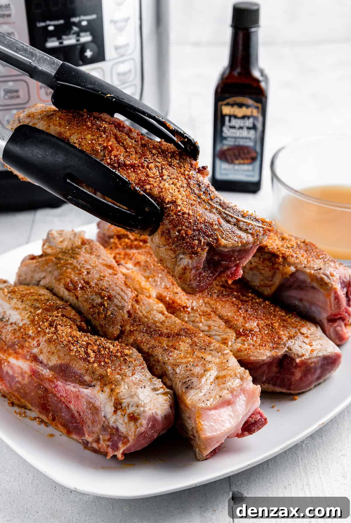 A Pair of Tongs Holding a Seasoned Pork Rib Over a Plate Full