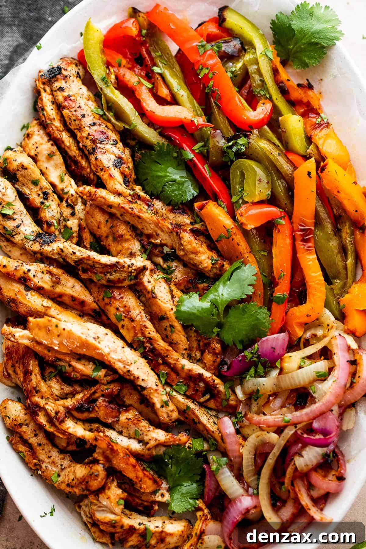 Easy grilled chicken fajitas featuring juicy chicken, onions, and peppers, served in warm tortillas with your favorite toppings. grilled chicken strips, colorful bell pepper strips, and onions on a serving plate garnished with cilantro leaves
