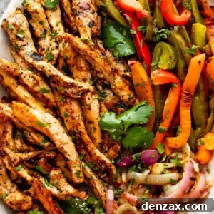 Smoky Grilled Chicken Fajitas with Peppers and Onions 2 grilled chicken fajitas with chicken strips, colorful bell pepper strips, and onions on a serving plate garnished with cilantro leaves