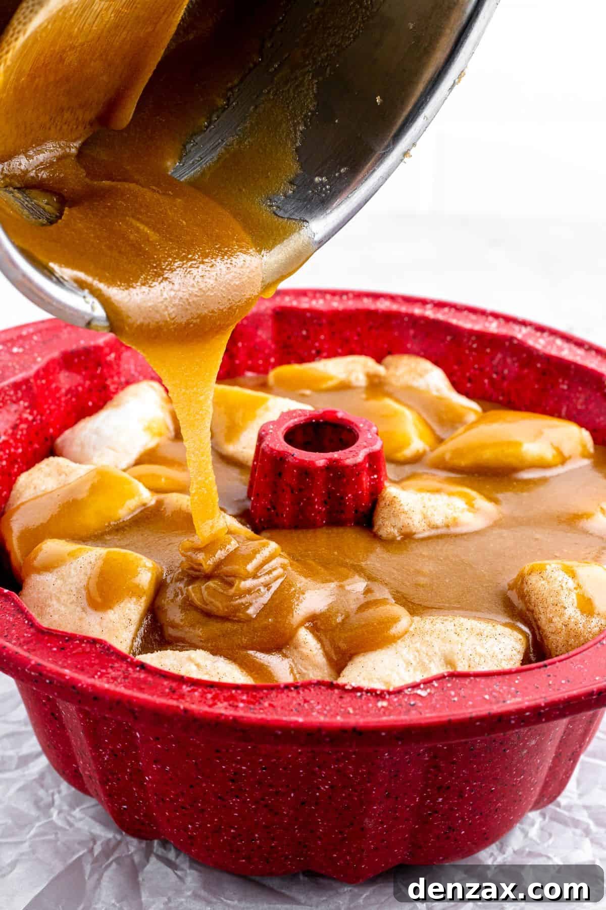 A thick brown-sugar-butter mixture is poured from a saucepan over biscuit dough pieces in a Bundt pan.