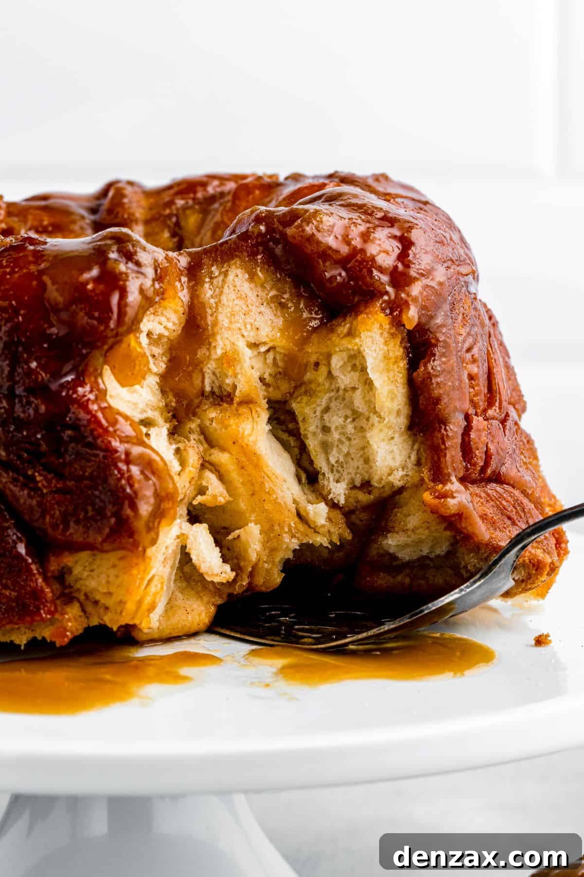 A baked monkey bread on a cake stand has several pieces removed and a cake server tucked underneath it.