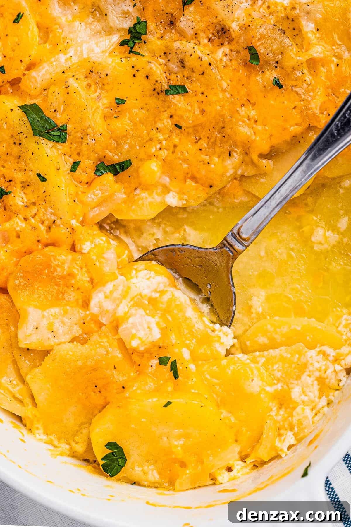 Tender sliced potatoes layered with cheddar cheese and diced onions to make a scalloped potatoes casserole. spoon scooping out scalloped potatoes from a white casserole dish