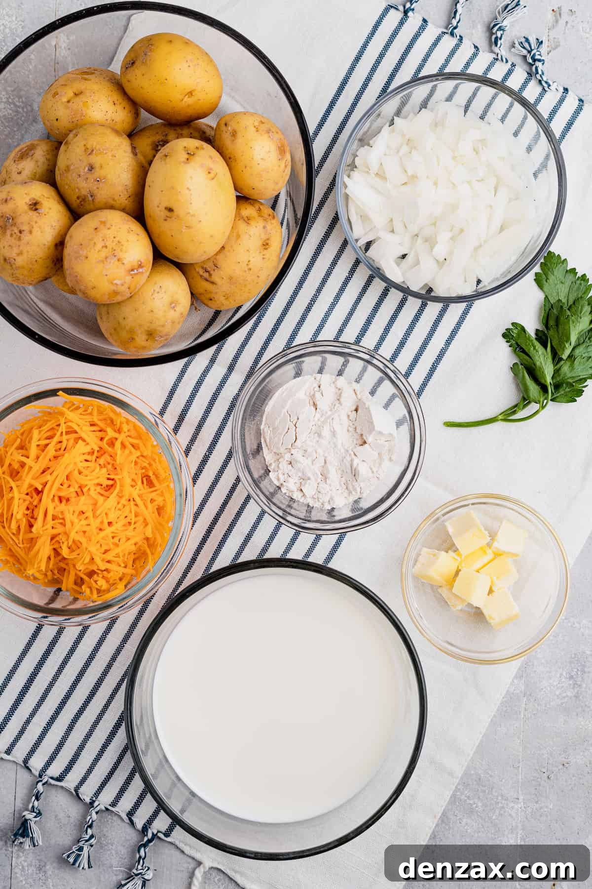 Tender sliced potatoes layered with cheddar cheese and diced onions to make a scalloped potatoes casserole. Clockwise from the top: diced onion, all-purpose flour, cubed butter, evaporated milk, shredded cheddar cheese, whole washed potatoes.