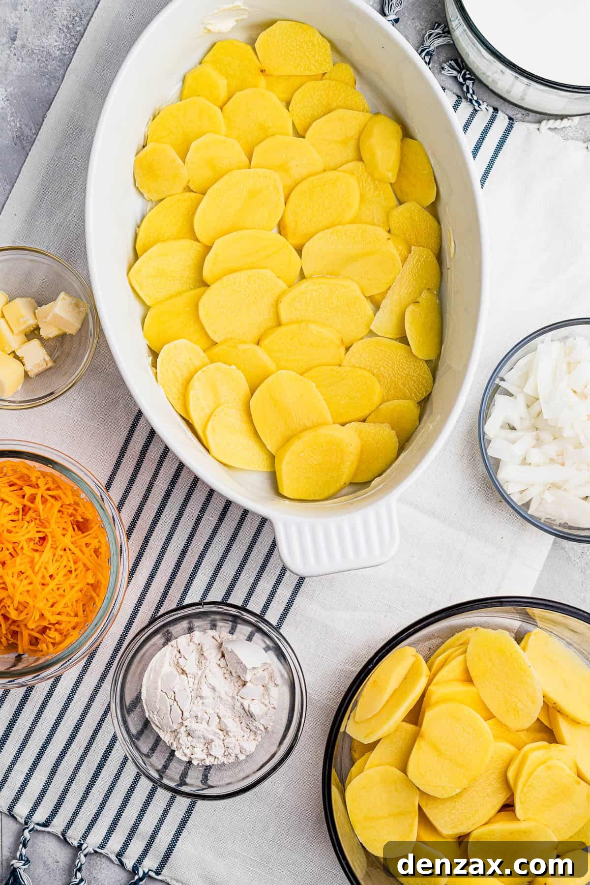 Tender sliced potatoes layered with cheddar cheese and diced onions to make a scalloped potatoes casserole. Sliced potatoes layered in a baking dish.