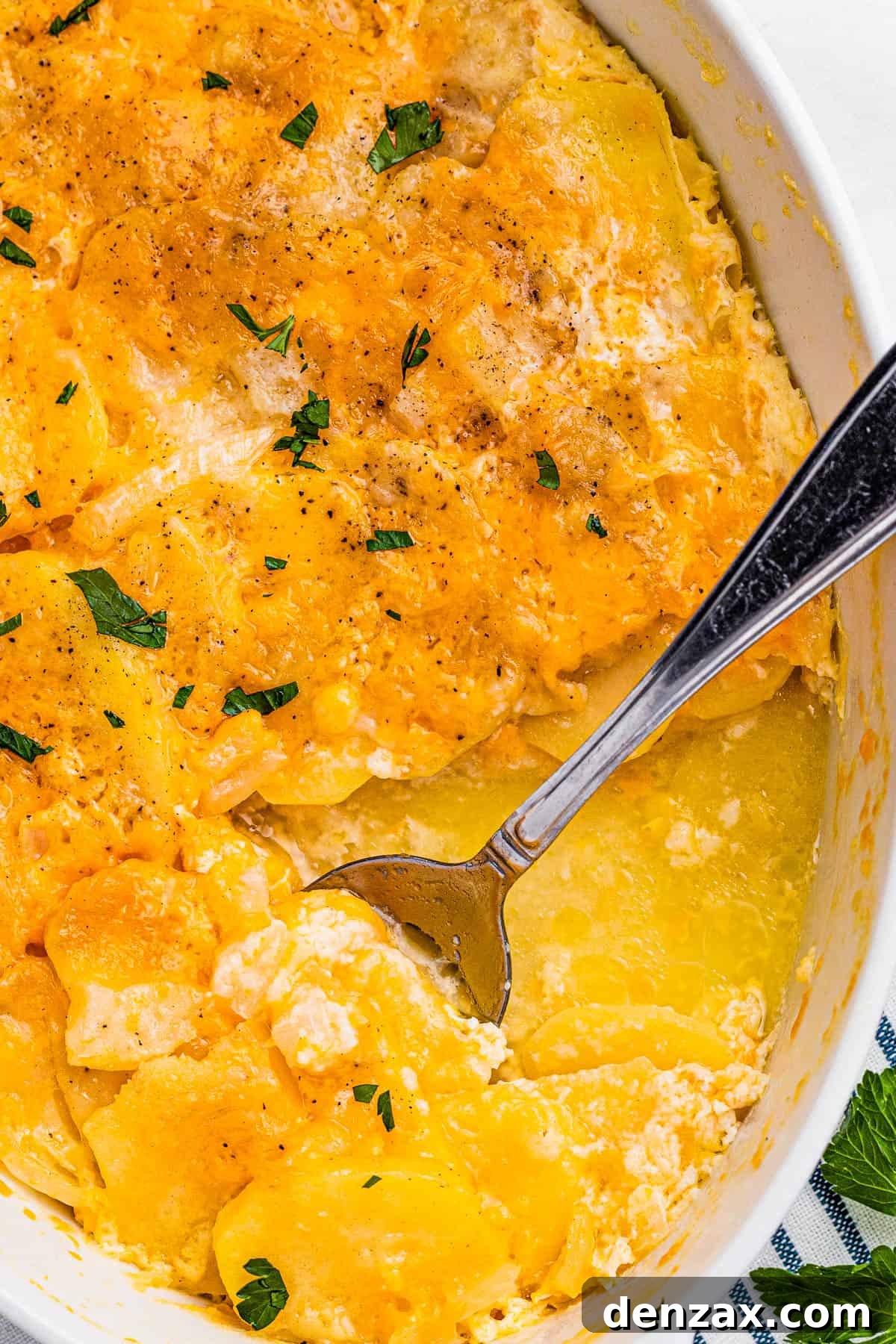 Tender sliced potatoes layered with cheddar cheese and diced onions to make a scalloped potatoes casserole. scalloped potatoes in a white casserole dish with a spoon inside the dish