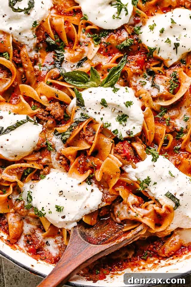 Skillet Lasagna ready to serve Close-up shot of curly pasta noodles in meat sauce, topped with melted cheese and chopped herbs.