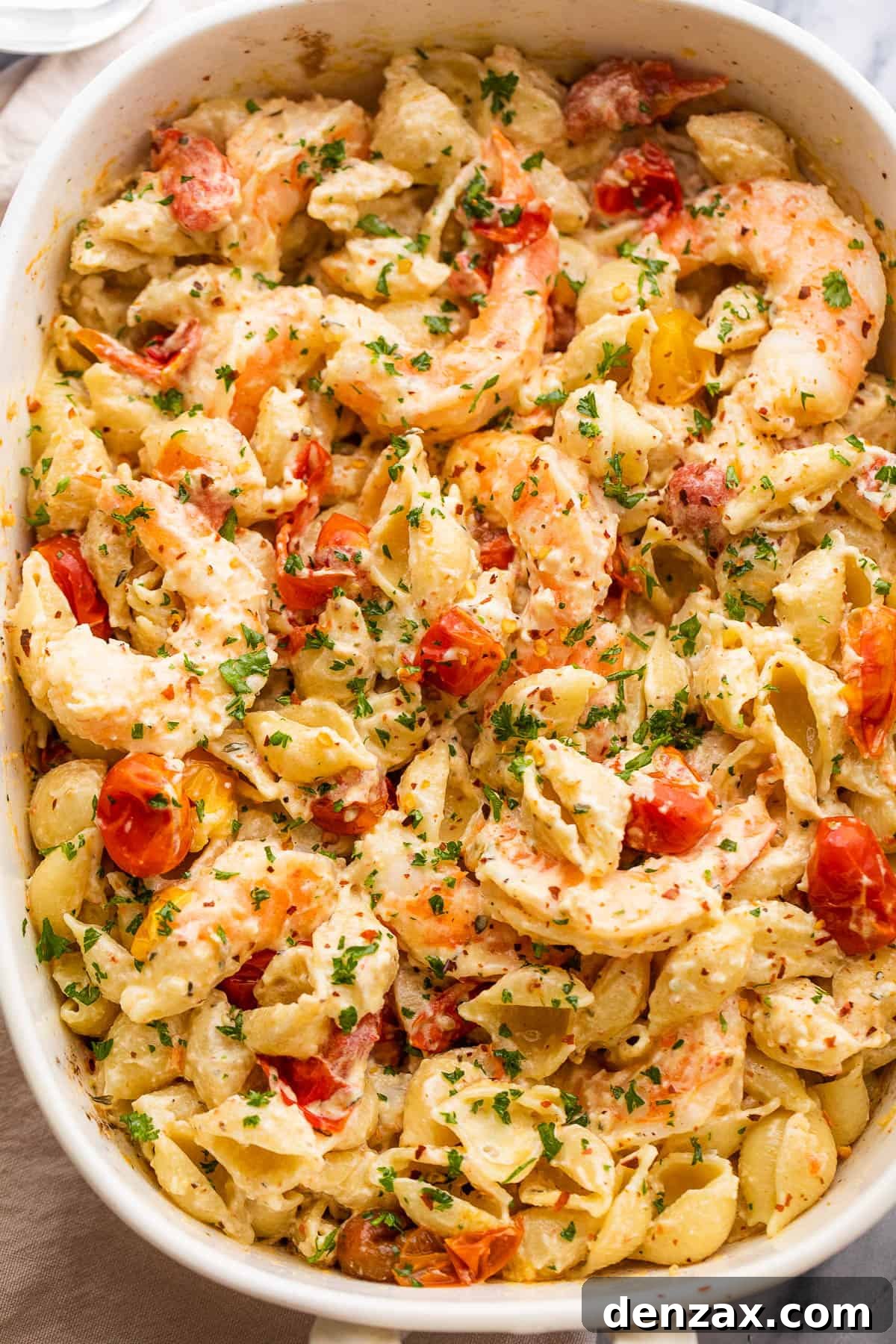 white baking dish with shrimp and pasta tossed with a cream cheese sauce and cherry tomatoes