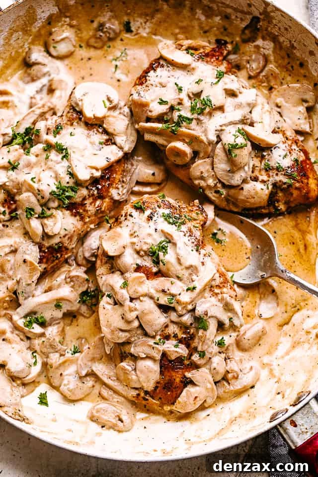 Creamy mushrooms spooned over chicken in a skillet garnished with fresh herbs