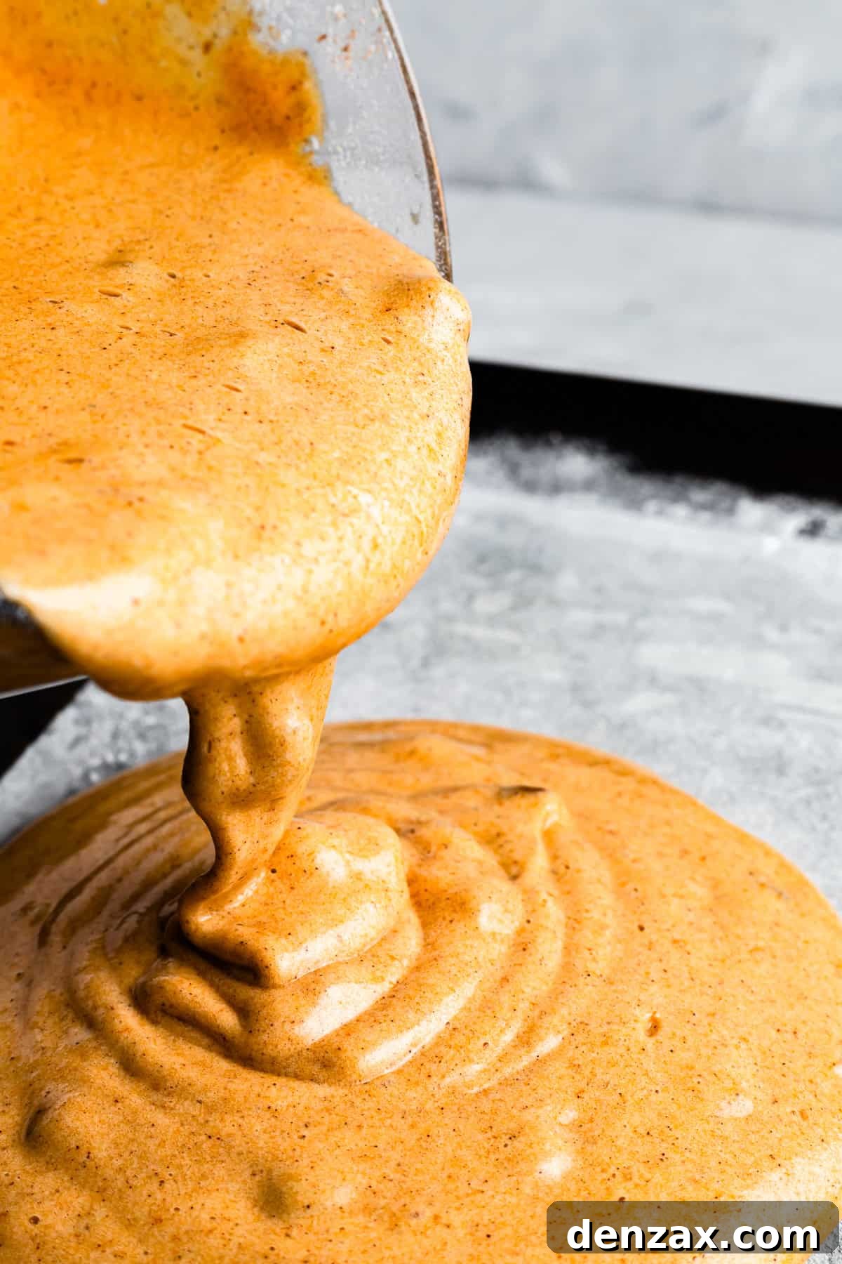 Pouring cake batter into a parchment paper-lined baking sheet.