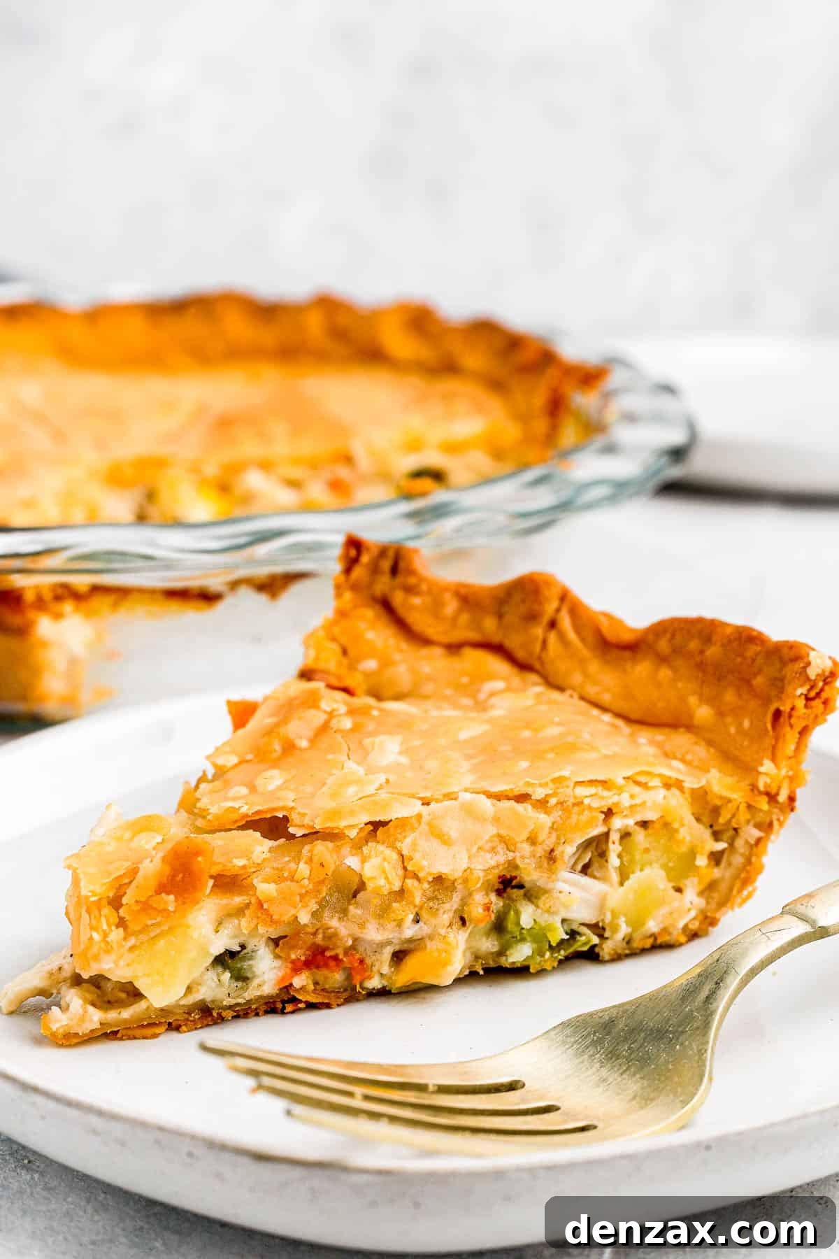 In the background, the baked chicken pot pie. In the foreground, a slice of the pie on a plate with a fork.