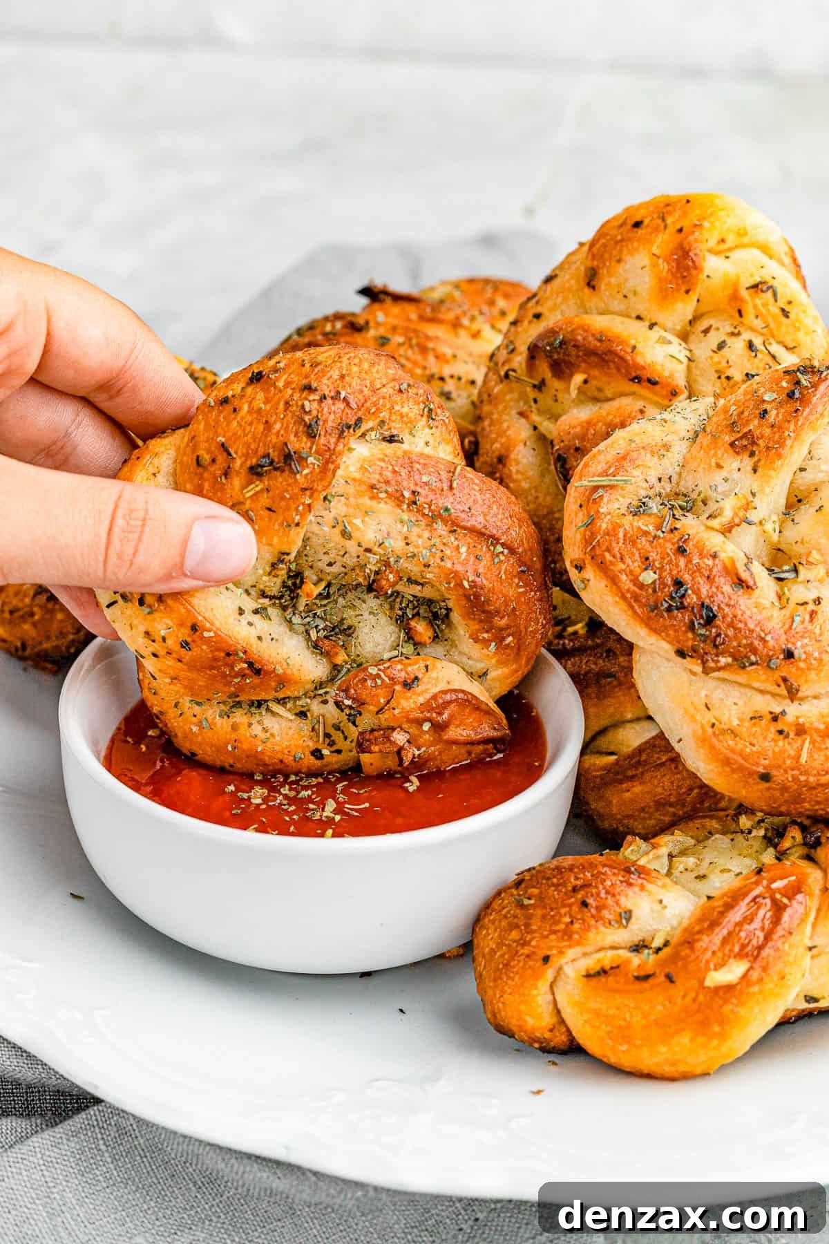 Easy Homemade Garlic Knots Recipe — Soft, Buttery & Ready in 30 Minutes 2 dipping garlic knots in marinara sauce.