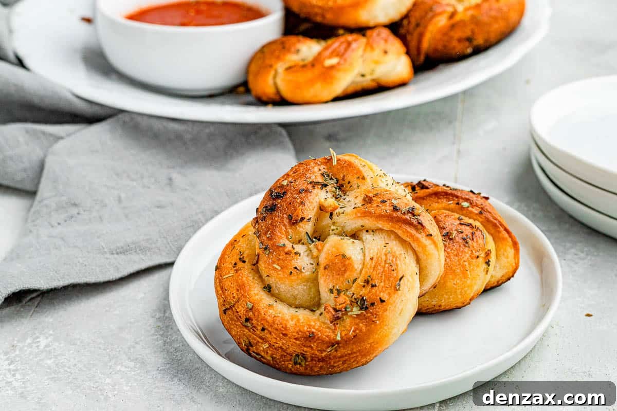 Easy Homemade Garlic Knots Recipe — Soft, Buttery & Ready in 30 Minutes 3 A wide shot of garlic knots piled onto a plate with marinara dipping sauce on the side.