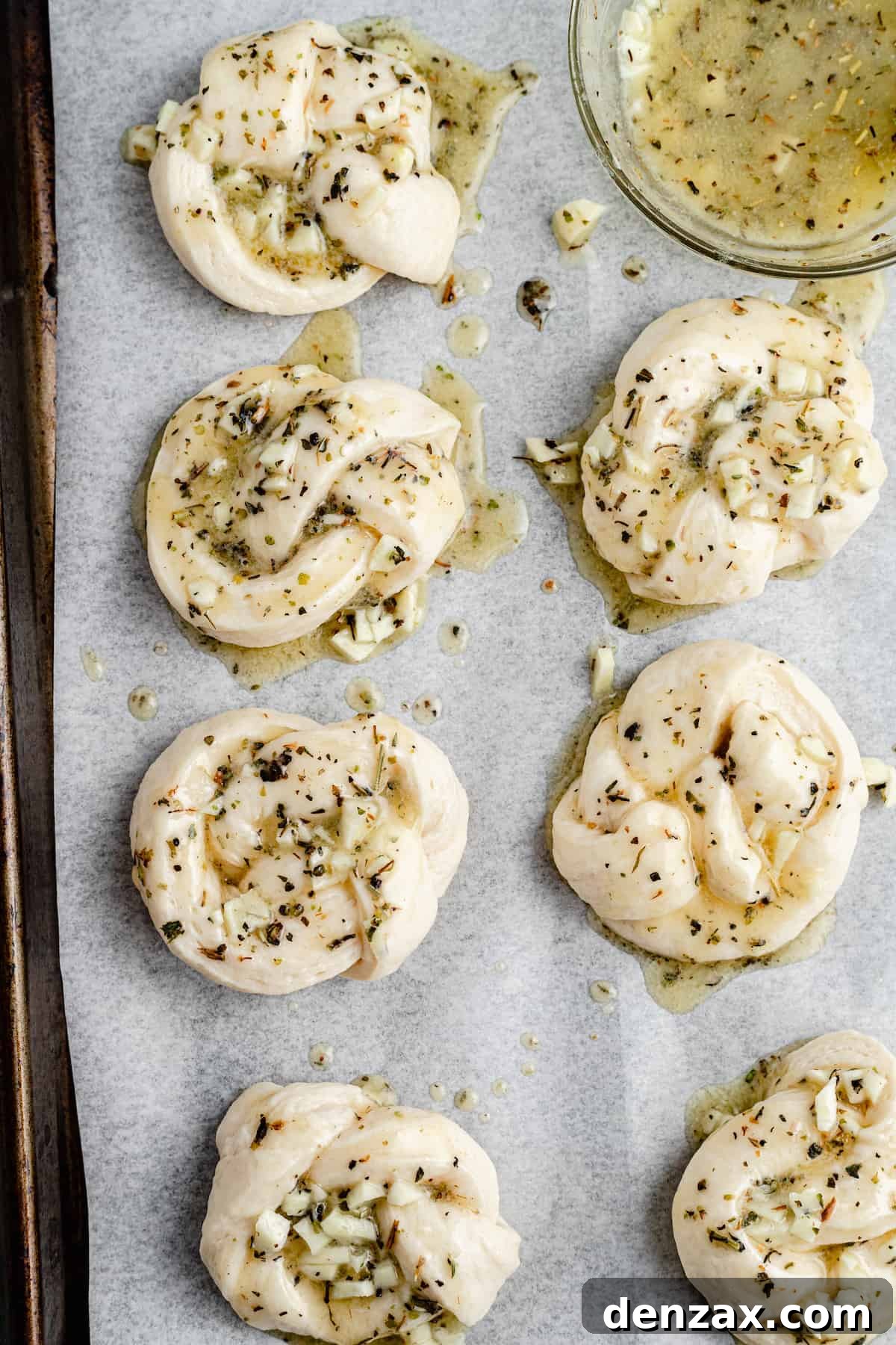 Easy Homemade Garlic Knots Recipe — Soft, Buttery & Ready in 30 Minutes 6 Unbaked garlic knots, brushed with garlic-and-herb-butter, on a parchment-lined tray.